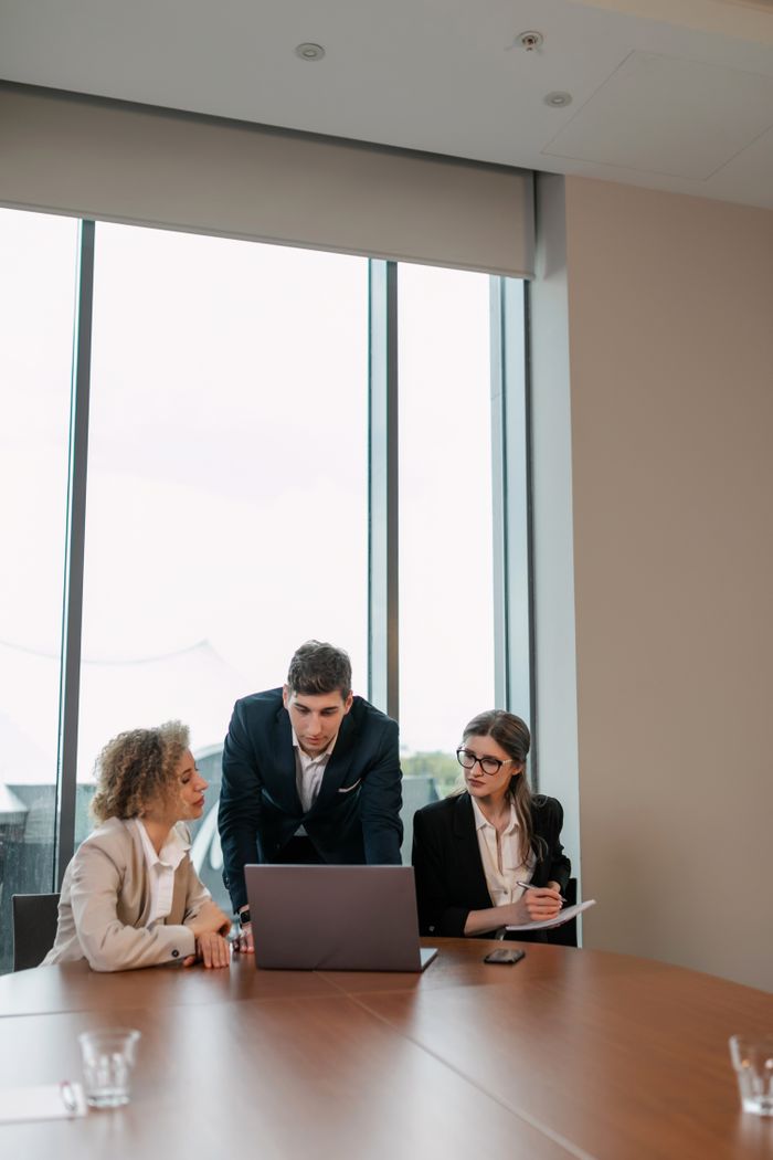 The Art of Drawing Readers In: Your attractive post title goes here Business professionals engaged in a meeting around a laptop in a modern office setting.